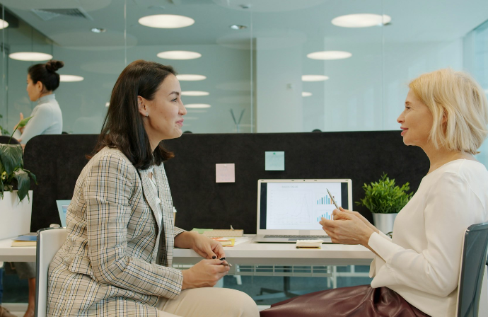 Two women talking at a desk in an office.